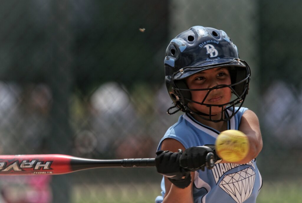 Girl wearing softball batting gloves hitting the softball